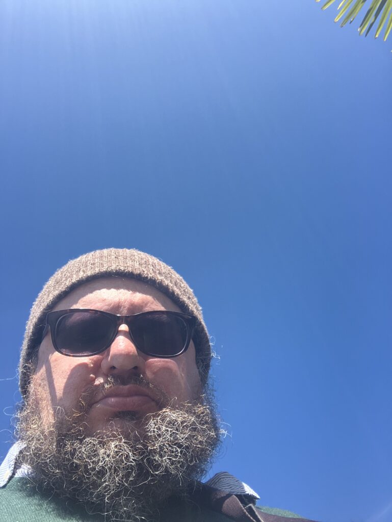 Carsten Weigelt mit Bart, Mütze und Sonnenbrille vor blauem Himmel